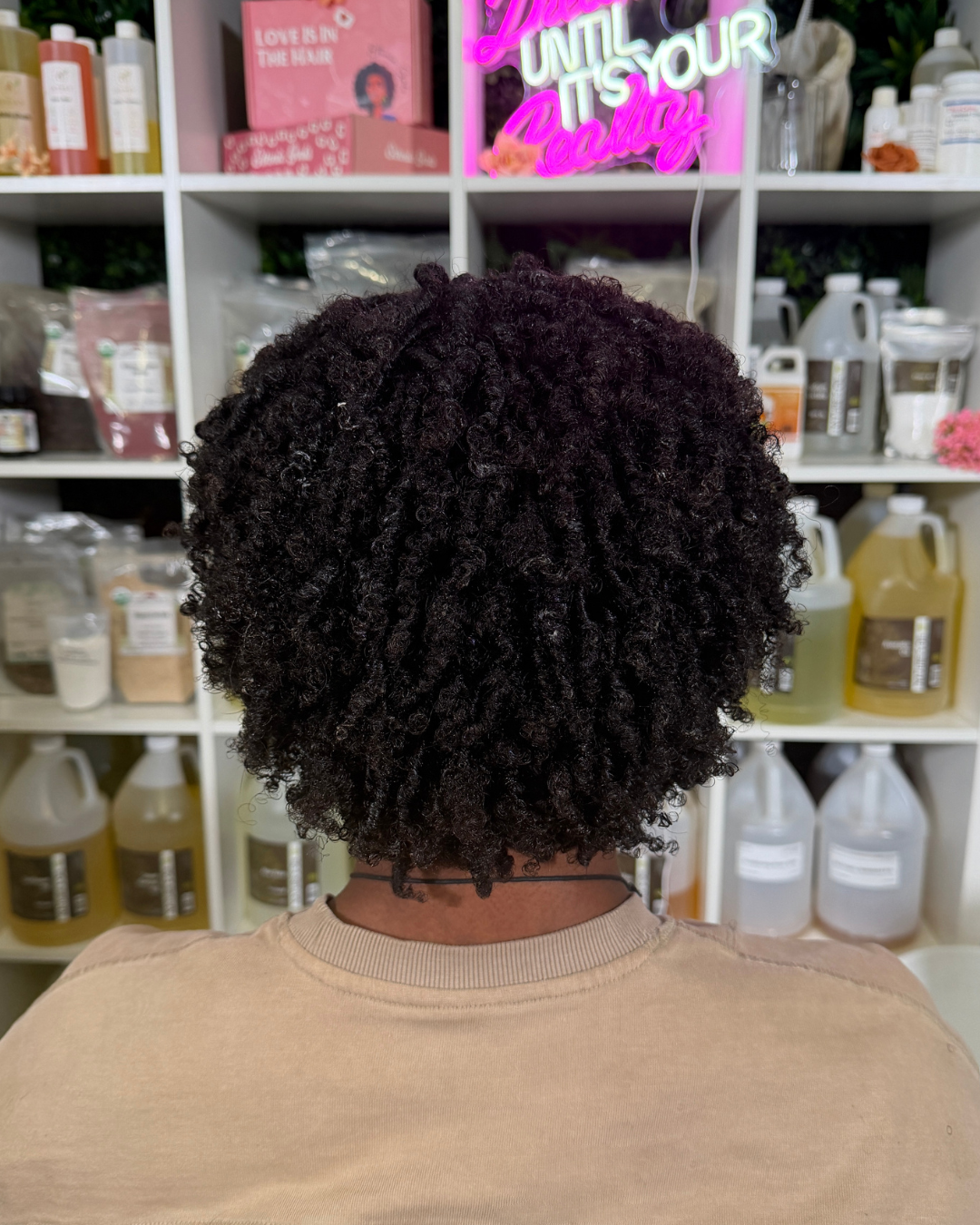 afro headed man with styled hair in a salon setting with shelves of ethnic gals porosity products.