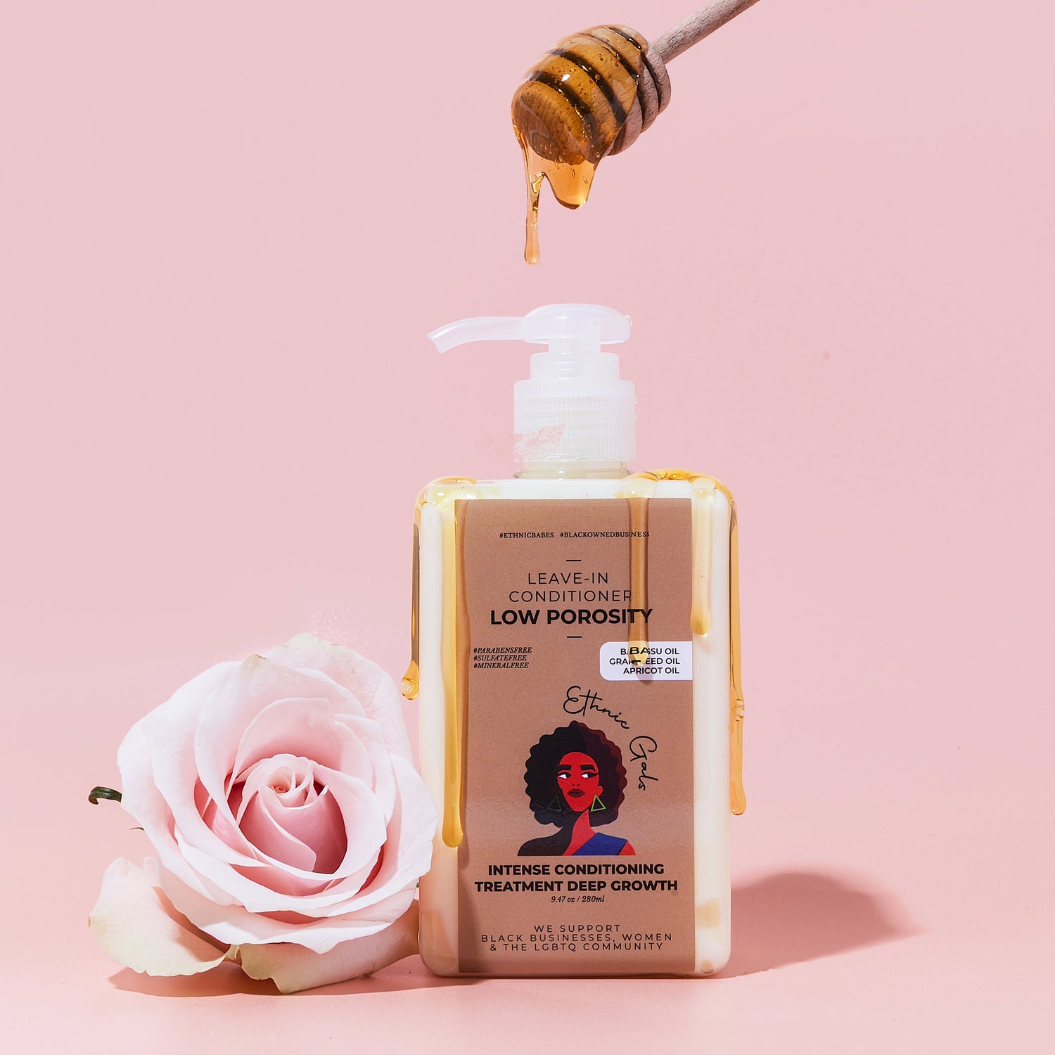 Bottle of hair care product with a honey dipper and pink rose on a pink background