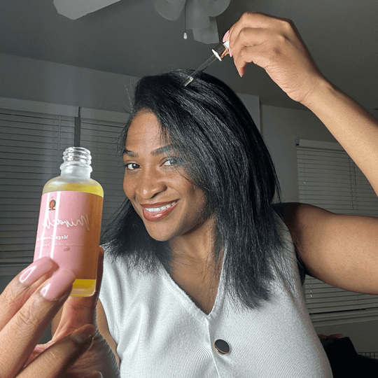 Woman holding a bottle of hair oil and a dropper in a room with a ceiling fan.