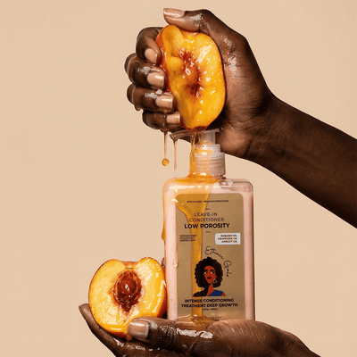 Hand holding a bottle of hair care product with peach slices on a beige background
