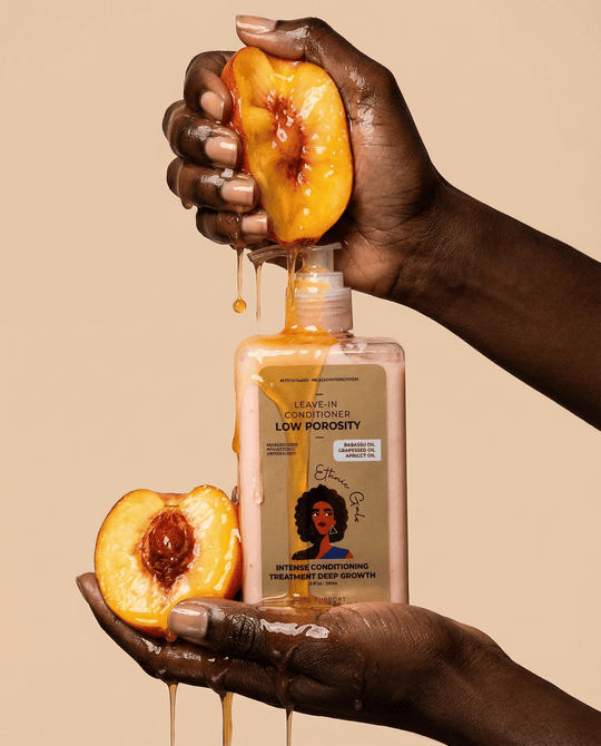Hand holding a bottle of hair care product with peach slices on a beige background