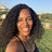 Woman with curly hair smiling outdoors with greenery and umbrellas in the background